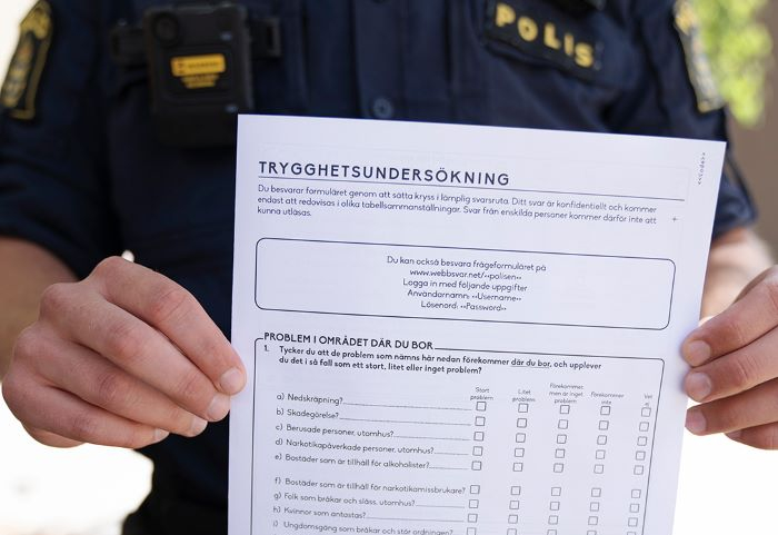 Polis i bakgrunden håller upp en sida från Trygghetsundersökning som skickas ut till invånare.