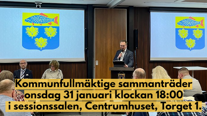 Kommunfullmäktige sammanträder i sessionssalen, Centrumhuset, onsdag 31 januari 2024 Information står med mörk text på gul bakgrund över bilden där man ser kommunfullmäktiges presidie och kommunens vapen på skärmar bakom.