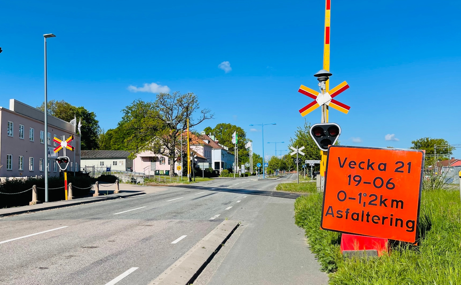 Vägskylt vid järnvägsövergång som informerar om att asfaltering görs på väg 21 under vecka 21.